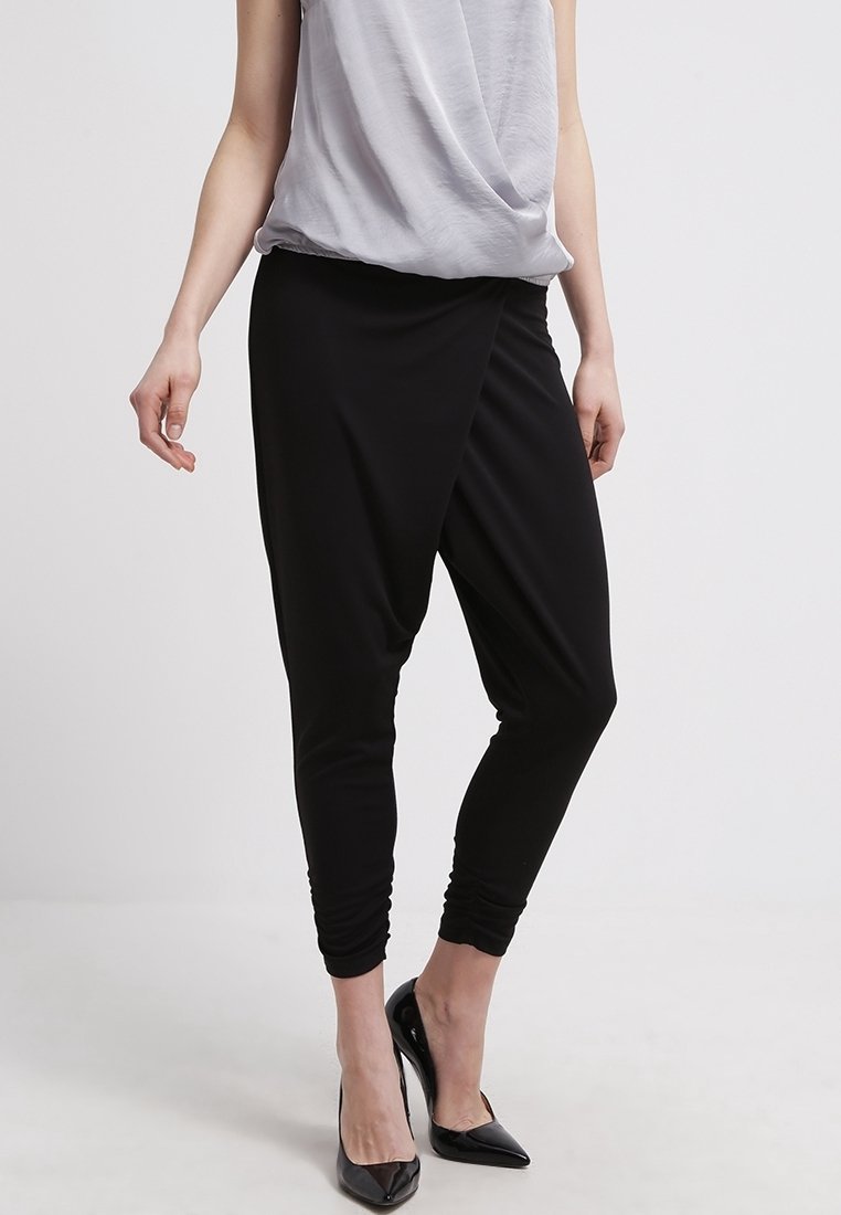Black draped harem pants with a tapered leg design, made of soft fabric, featuring a smooth texture and a relaxed, loose fit around the waist.