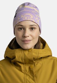 Purple beanie with a light pattern and a logo tag, made from knitted fabric. Worn with a yellow, insulated jacket featuring a stand-up collar.