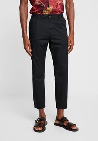 Pantaloni in cotone neri con una vestibilità slim, dotati di tasche laterali e chiusura con bottone, abbinati a sandali marroni. Design leggero e strutturato.