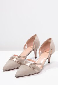 Beige suede high heels with pointed toes, metallic accents, and open sides. Slim heels and a smooth inner lining complete the design.