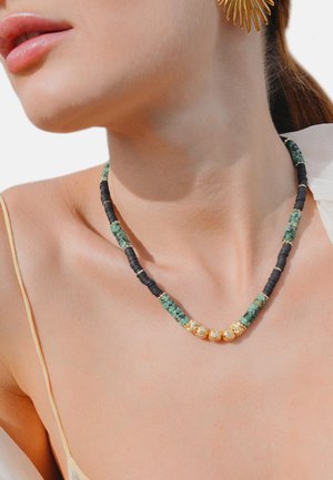 Collier en perles avec des sections en pierre verte et en caoutchouc noir, rehaussé de perles dorées. Texture lisse, design incurvé, ajusté.