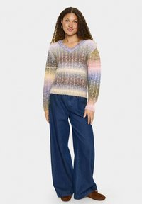 Krāsains adīts džemperis ar V veida dekoltē, ar horizontālām svītrām pasteļtoņos. Apvienots ar plaša griezuma džinsu biksēm un brūnām kurpēm.
