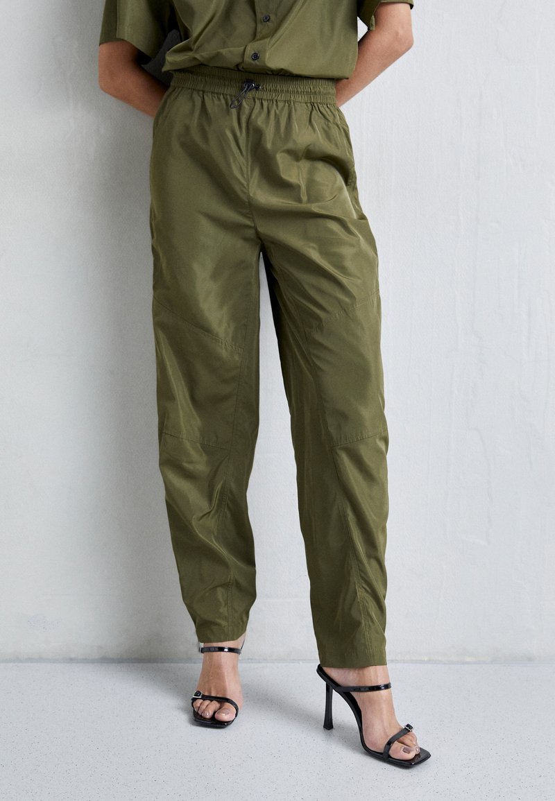 Olijfgroene, lichtgewicht broek met elastische tailleband en een relaxte pasvorm. Voorzien van zijzakken en een smooth, licht glanzende textuur.