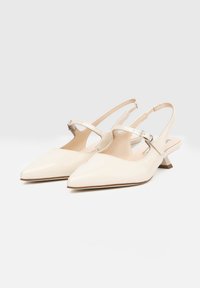 Scarpe slingback in pelle verniciata beige con punta affusolata, tacco a blocco corto e cinturini alla caviglia regolabili con fibbia argentata.