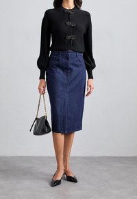 Svart ribbad långärmad topp med tre dekorativa knappar, matchad med en mörk denim penkjol och svarta spetsiga pumps. Svart handväska.