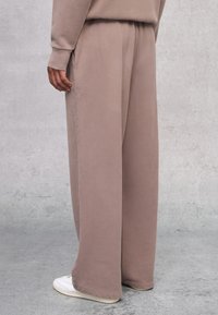 Pantalones de pierna ancha en un suave tejido topo, con textura lisa, cinturilla elástica y bolsillos laterales, combinados con zapatillas deportivas blancas.