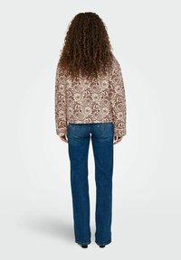 Skraćeni, uzorkovani kaput u krem i maroon boji s paisley uzorkom, uparen s plavim bootcut trapericama. Tkanina izgleda teksturirano.
