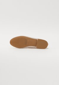 Scarpa piatta trasparente con parte superiore traslucida caratterizzata da piccoli ritagli circolari, una suola in gomma marrone testa di moro texture e una punta arrotondata.