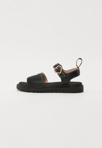 Sorte skinnsandaler med flat såle, åpen tå, justerbar rem med hjerteformet dekorasjon, samt beige sømdetaljer.