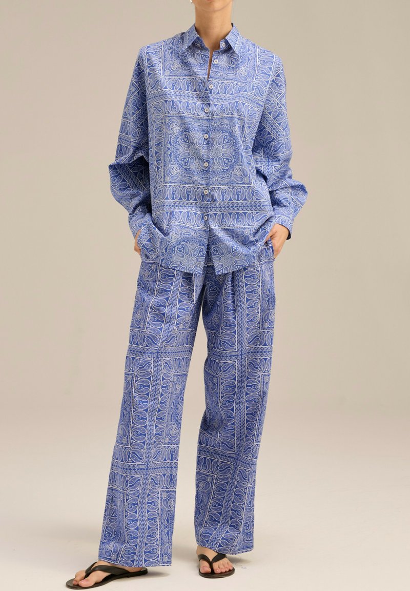 Niebieska koszula zapinana na guziki w wzory i dopasowane szerokie spodnie wykonane z lekkiego materiału, charakteryzujące się misternymi wzorami i luźnym krojem.