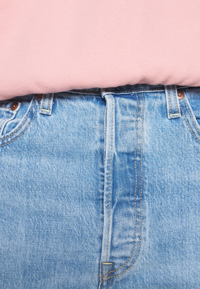 Helles pinkes Sweatshirt über einer hellblauen Jeans. Die Jeans verfügen über einen Reißverschluss, Taschen und Steppnähte.