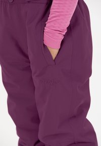 Lila wasserdichte Hose mit matter Oberfläche, ausgestattet mit einer Seitentasche und einem geprägten Logodetail, kombiniert mit einem pinkfarbenen strukturierten Langarmoberteil.