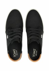 Sneakers in tela nera con suole in gomma bianca, punta rotonda e sei fori per i lacci. Presentano un accento sul tallone marrone e il marchio TOMS sulla soletta.