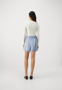 Pantaloni corti blu chiaro con strisce verticali, dotati di una vita piatta e pieghe posteriori. Il materiale sembra liscio, abbinato a scarpe con tacco a blocco nere.