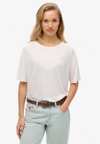 Camiseta de manga corta color rosa claro, hecha de una tela suave, con un escote redondo y un corte relajado, combinada con unos vaqueros claros y un cinturón marrón.