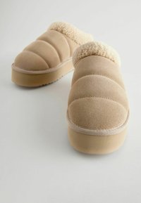 Chaussons beiges en tissu doux avec un col en fourrure pelucheux, présentant un design rembourré et une semelle plateforme modérée.
