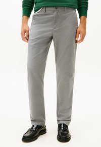 Pantalons gris avec une texture de tissu lisse, comportant des passants de ceinture et des poches avant, associés à des chaussures en cuir noires.