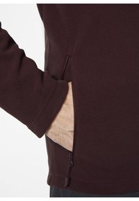 Burgundowy polarowy sweter z boczną kieszenią na zamek. Charakteryzuje się gładką teksturą i dopasowanymi rękawami z przeszyciem na nadgarstku.
