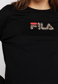 Černé tričko s krátkým rukávem s barevným logem FILA v designu leopardího vzoru s červenými akcenty na písmenech. Měkký bavlněný materiál.