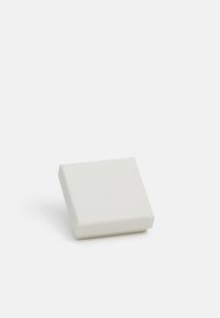 Boîte carrée blanche avec une surface texturée et des bords arrondis, présentant un logo en relief subtil sur le dessus.