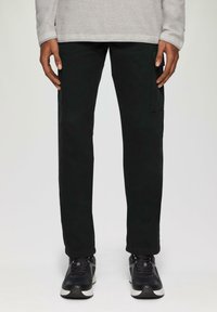 Zwarte cargo broek met een rechte snit, voorzien van zijzakken. Gecombineerd met zwarte sneakers en een lichtgrijze long-sleeve top.