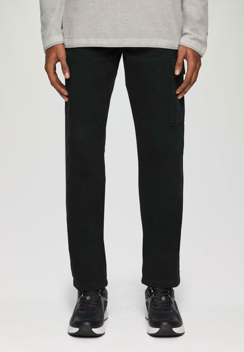 Zwarte cargo broek met een rechte snit, voorzien van zijzakken. Gecombineerd met zwarte sneakers en een lichtgrijze long-sleeve top.