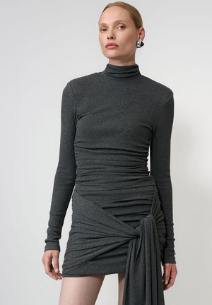 Szara sukienka z długim rękawem, z kołnierzem typu mock turtleneck, marszczonym materiałem i akcentem w postaci bocznego drapowania, wykonana z miękkiego, elastycznego materiału.