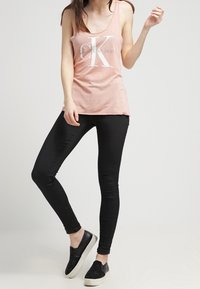 Rosa linne med vit "Calvin Klein Jeans" logotyp, parat med svarta skinny jeans och svarta slip-on skor med vita sulor.
