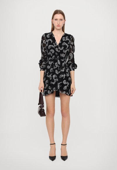 Zwarte doorzichtige jurk met zilveren paisleypatroon, V-hals, lange puffmouwen, Taille cinched, en een licht uitlopende rok. Paar zwarte pumps.