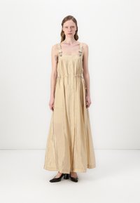 Maksi haljina u svijetloj bež boji, izrađena od sjajne tkanine. Ima podesive naramenice, struk s vezicom i dugačak je kroj s labavim fitom.