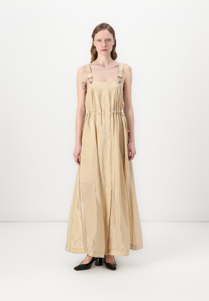 Vestido maxi em bege claro, feito de tecido brilhante. Apresenta alças ajustáveis, cintura com cordão e é de comprimento até ao chão com um corte solto.