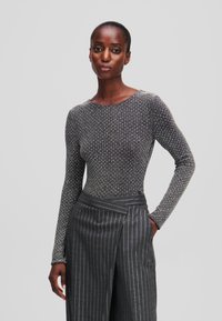 Garais piedurknēm, piegulošs tops melnā krāsā ar metāliskiem punktiņiem. Saskaņots ar pelēku svītrainu biksēm ar aplokšņu dizainu.