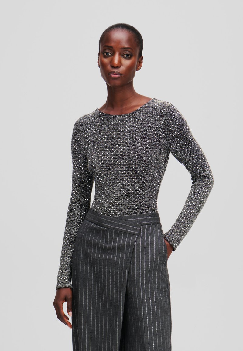 Garais piedurknēm, piegulošs tops melnā krāsā ar metāliskiem punktiņiem. Saskaņots ar pelēku svītrainu biksēm ar aplokšņu dizainu.