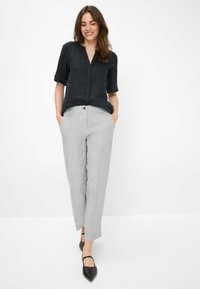 Zwarte, mouwloze shirt met een V-halsontwerp en knoopdetails, gecombineerd met lichtgrijze, op maat gemaakte, rechte broek en zwarte puntige schoenen.