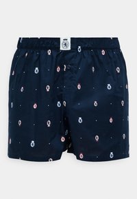 Mørkeblå boxershorts med elastisk talje, prydet med et gentaget mønster af små emblemeter i rød, blå og hvid. Knaplukningsdetalje.