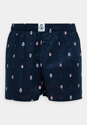 Boxers azul marino con cinturilla elástica, que presentan un patrón repetitivo de pequeños emblemas en rojo, azul y blanco. Detalle de cierre con botón.