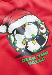 Hanorac roșu cu un grafic care reprezintă o minge de fotbal purtând o pălărie de Moș Crăciun, împodobită cu luminițe de Crăciun colorate și textul "DECK THE BALLS."