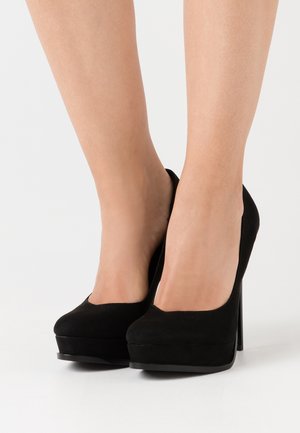 Chaussures à talons hauts noires avec une texture en daim, bout rond et semelle plateforme, présentant un design élégant et un haut talon aiguille.