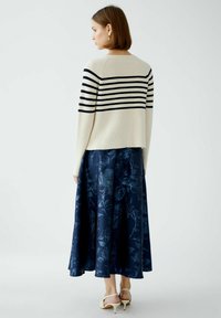 Knitpullover in Creme mit schwarzen horizontalen Streifen, kombiniert mit einem langen marineblauen Rock mit floralem Muster und hellen Absatzschuhen.