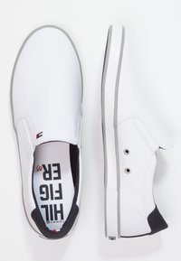 Scarpe slip-on bianche in tela con suola in gomma grigia, dotate di una soletta interna nera, due fori laterali e una soletta stampata.