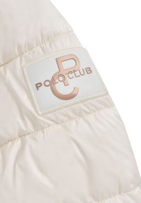 Kremowa, pikowana część kurtki z prostokątną białą naszywką z wypukłym, miedzianym napisem "PC" i "POLO CLUB".
