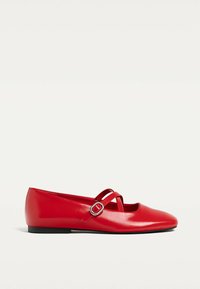 Ballerines rouges en cuir lisse. Jardins croisés avec une boucle en accent. Bout arrondi et semelle plate noire.