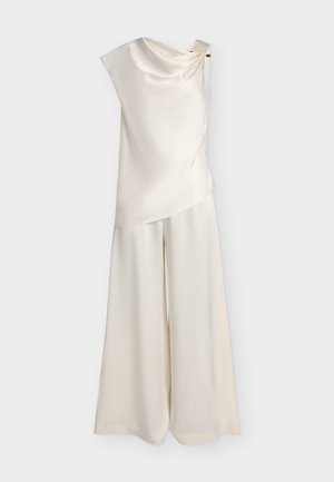 Haut en satin sans manches couleur crème avec encolure drapée et pantalon large assorti sur fond uni.