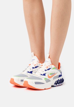 Scarpe da corsa Nike bianche, arancioni, blu e verdi indossate ai piedi, con tomaia in mesh e suola ammortizzata con fori di ventilazione.