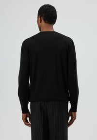 Zwarte gebreide trui met lange mouwen, geribbelde manchetten en een ronde hals, gecombineerd met gestreepte broek. Gestructureerde stof, casual ontwerp.