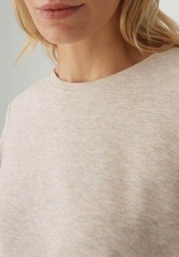 Beige geribbelde trui met een ronde halslijn en zachte textuur, met subtiele kleurschakeringen en een minimalistisch ontwerp.