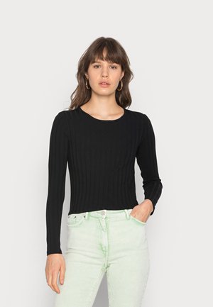 Top preto com textura e mangas longas, com um decote redondo, combinado com calças de veludo cotelê texturizadas em verde claro. Design simples e silhueta justa.
