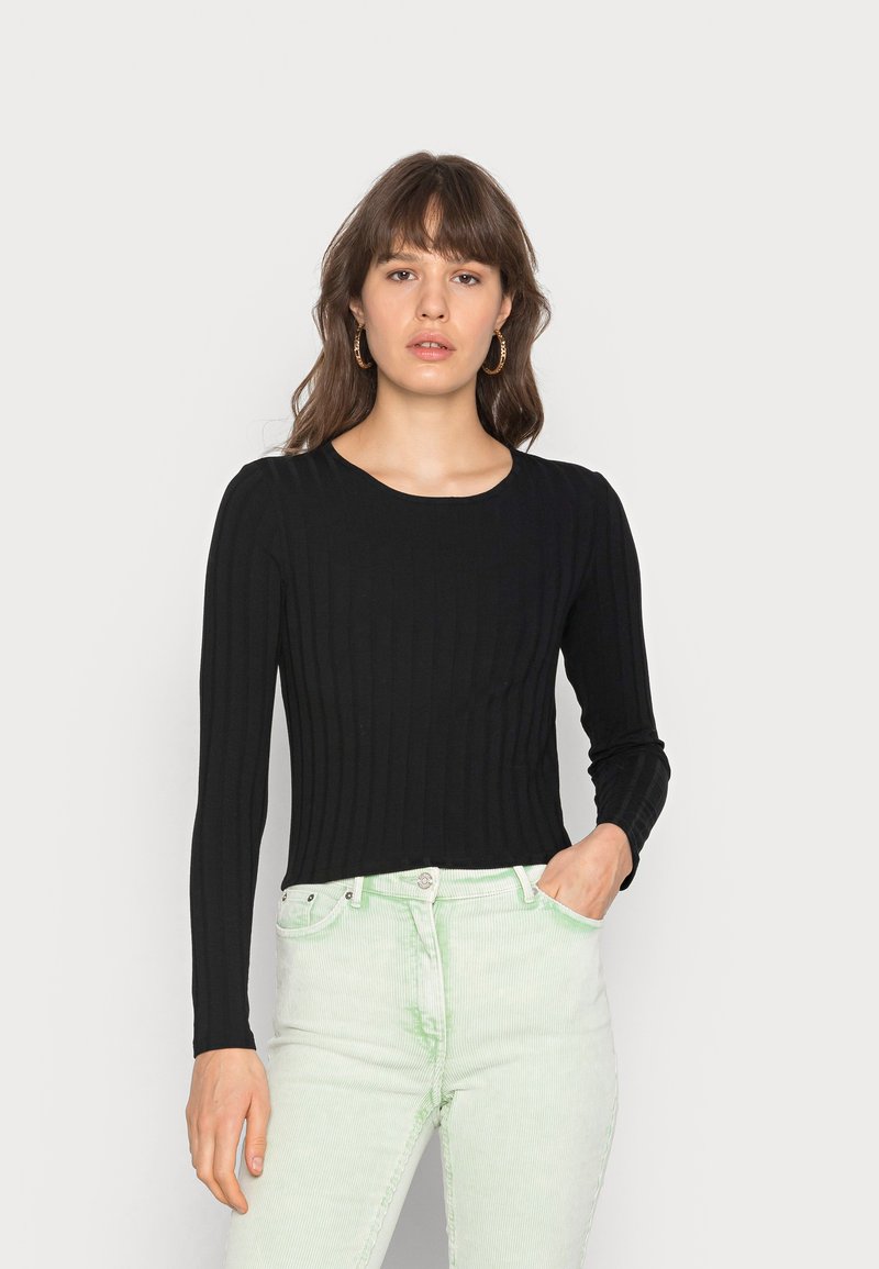 Top preto com textura e mangas longas, com um decote redondo, combinado com calças de veludo cotelê texturizadas em verde claro. Design simples e silhueta justa.