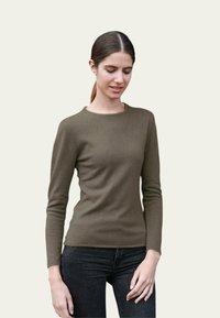 Un pull vert olive à manches longues en matériau doux, avec un col rond et une coupe ajustée, associé à un jean foncé.
