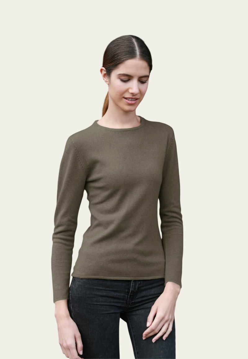 Un pull vert olive à manches longues en matériau doux, avec un col rond et une coupe ajustée, associé à un jean foncé.